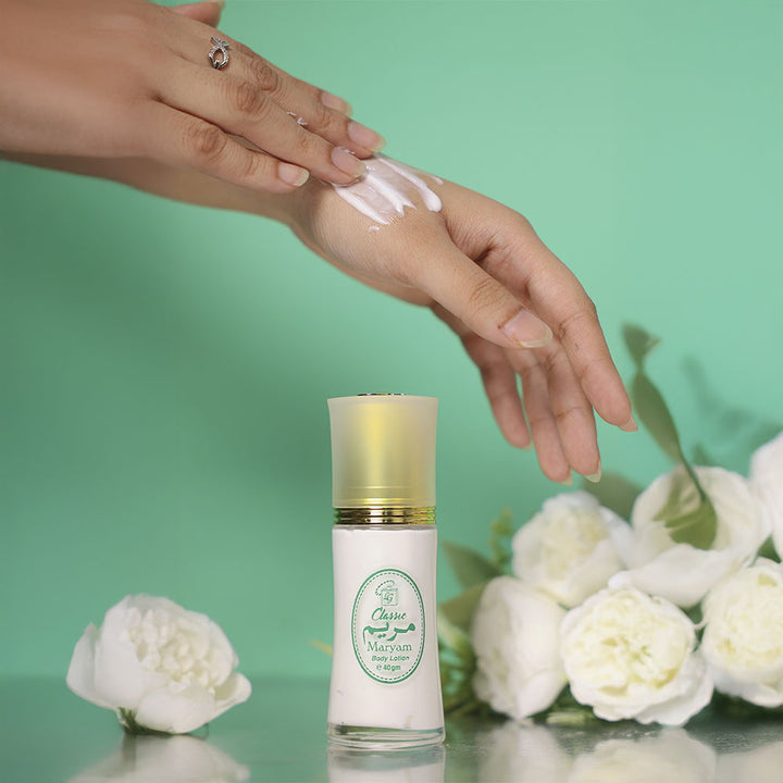 Hand applying maryam body lotion to another hand with a bottle of cream and white flowers on a green background