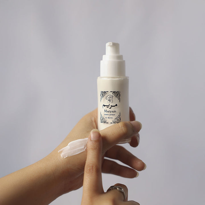Hand holding a bottle of Maryam skincare cream with a gray background